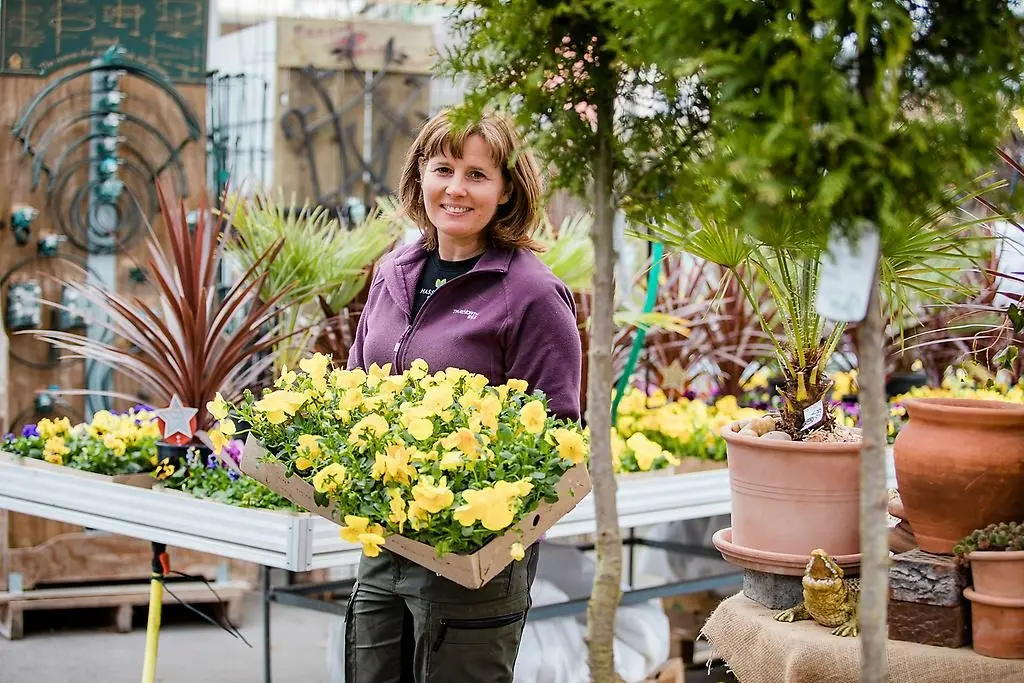 Glad kvinna som står med ett stort fång gula blommor i händerna.