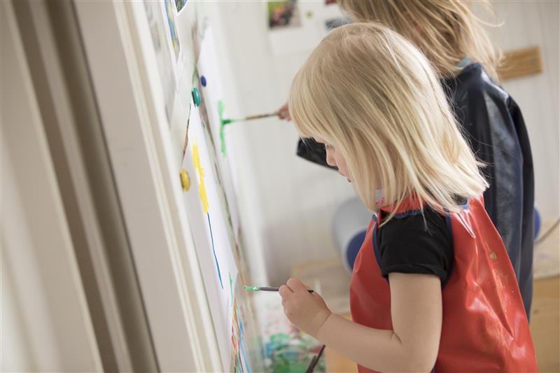 Två barn som målar med vattenfärger på papper upphängt på en vägg.