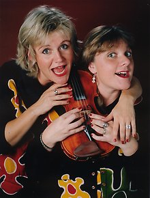 Två glada kvinnor med en fiol mellan sig.