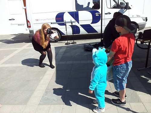 En kille med en cowboyhatt och en pojke utklädd i turkos mjukisdräkt fotograferas av en kvinna som hukar sig för att få rätt vinkel.