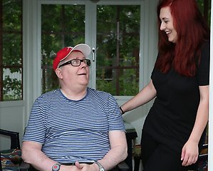 En kvinna ler och håller om en man sittande i rullstol.
