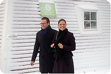 Kronprinsessan Victoria och Prins Daniel framför ett snötäckt hus med skylten Info Point Kinnekulle.