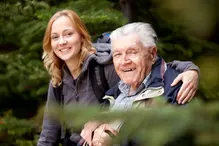 En kvinnlig vårdare håller om en äldre man med käpp.