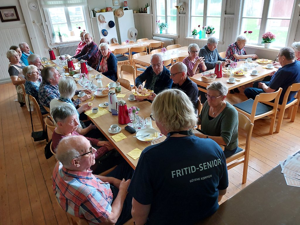 Deltagare på Fritid Senior sitter runt långbord, äter och umgås.
