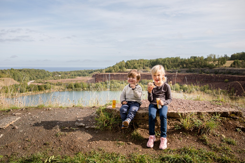 Två små barn fikar med ett stenbrott och en sjö i bakgrunden. 