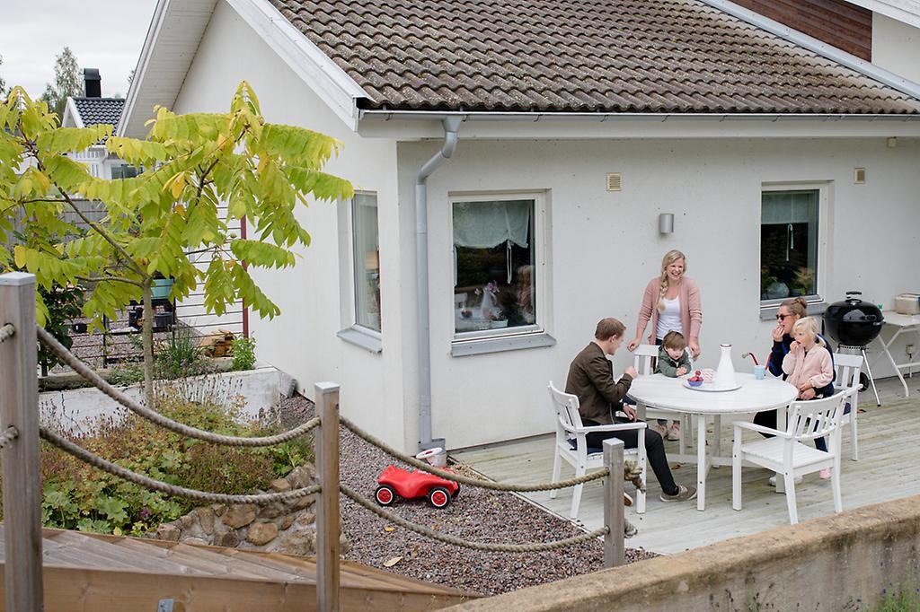Tre vuxna och två barn som fikar på altanen till ett hus.