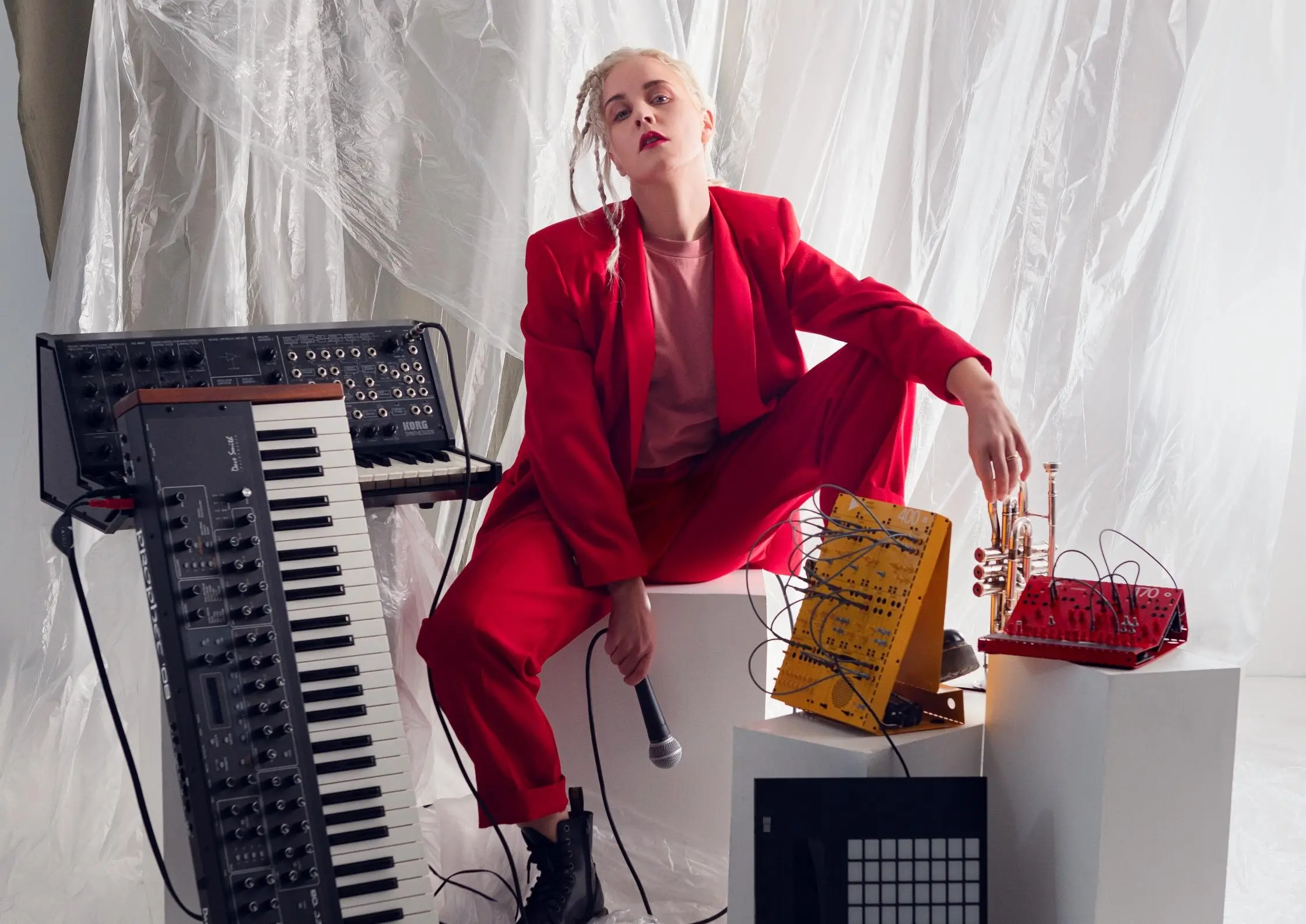 Kvinna i röd kostym som sitter bredvid en synt och håller i en mikrofon.