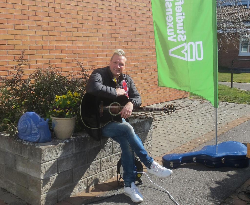 En blond man med gitarr sitter och ler mot kameran.