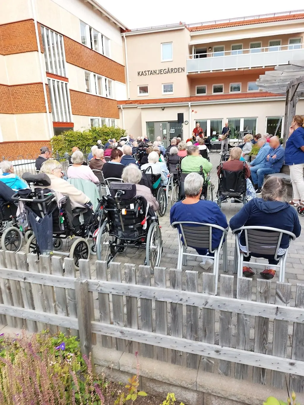 Äldre människor i ett publikhav framför scenen där två killar spelar och sjunger.