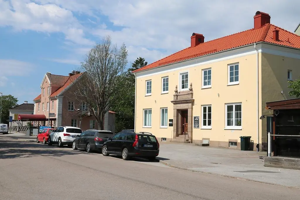 En bild som visar två äldre byggnader med putsade fasader längs en gata där bilar står parkerade.