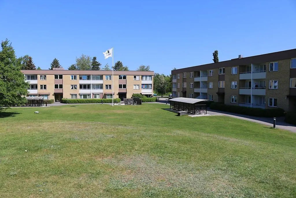 En bild som visar två flerbostadshus placerade i vinkel med en gräsmatta och kulle i förgrunden.