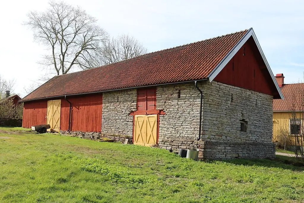 En bild som visar en ladugård i kalksten och rödmålat trä.