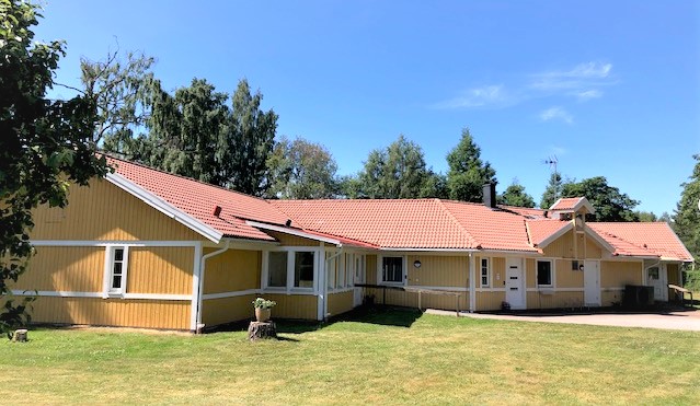 Nygården, ett gult hus med orange tegeltak. En grön gräsmatta på framsidan. 