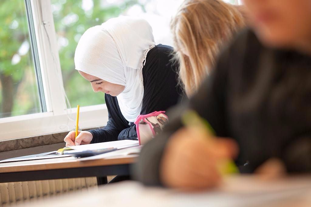 En kvinnlig elev med hijab antecknar i ett klassrum.