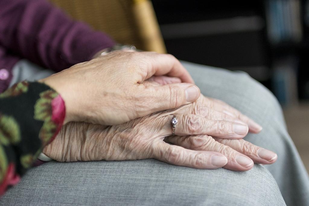 En kvinnas hand håller om en äldre kvinnas hand som vilar på hennes ben.