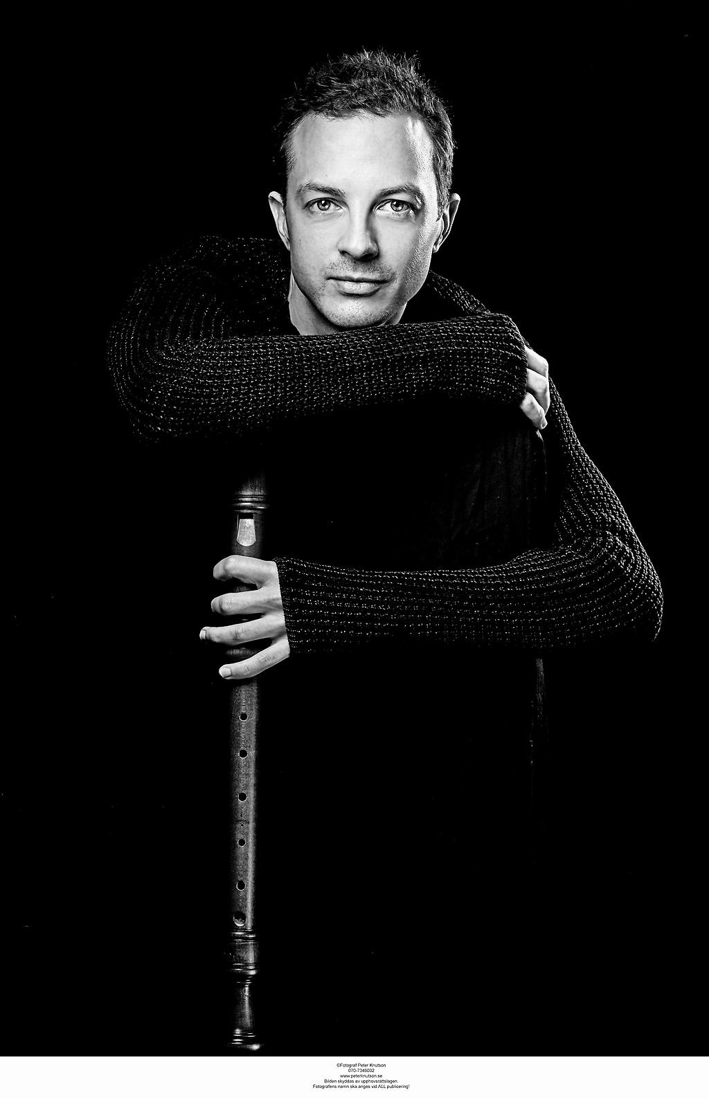Svartvit porträttbild på Per Gross som håller en blockflöjt i handen med en mörk bakgrund.