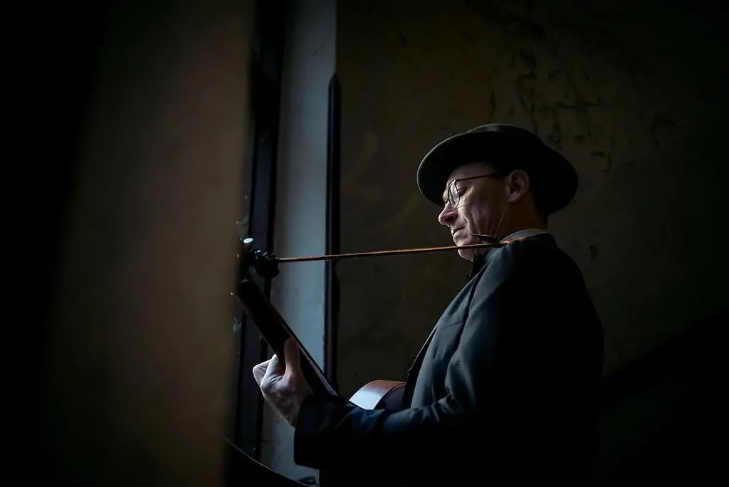 Man i hatt står vid en fönster och spelar gitarr.