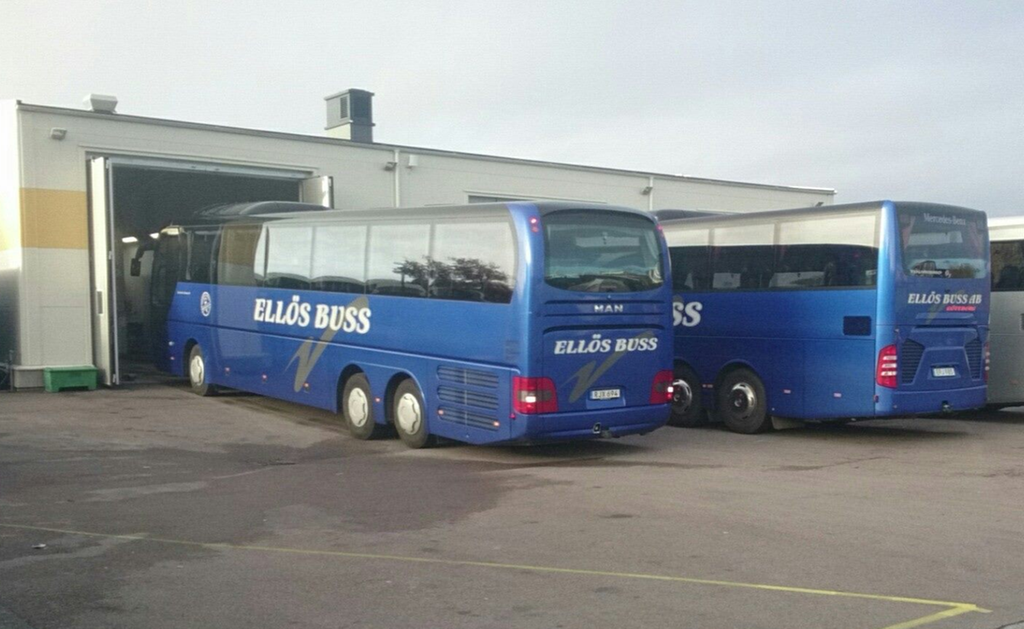 Två parkerade bussar med texten Ellös buss på sidan vid ett bussgarage.