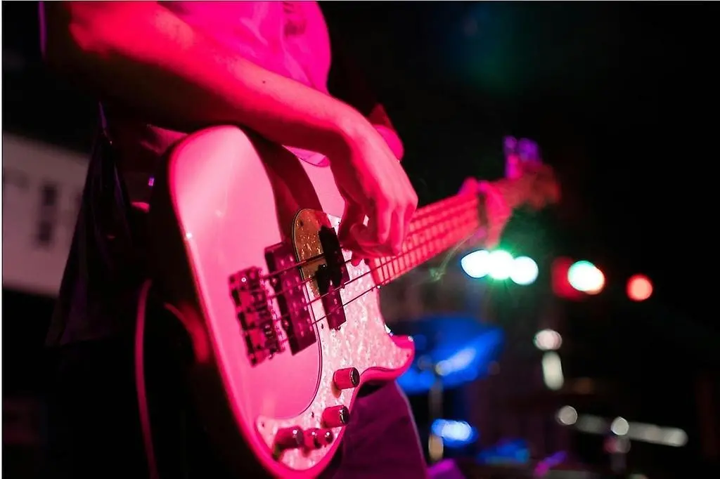 Person spelar på en elbas i rosa ljussken