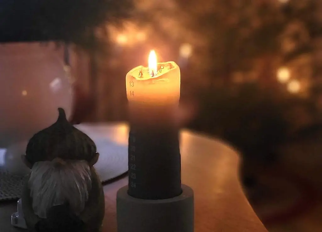 Ett tänt adventsljus med siffror står på ett bord. Bredvid står en prydnadstomte med vitt skägg och grå luva.