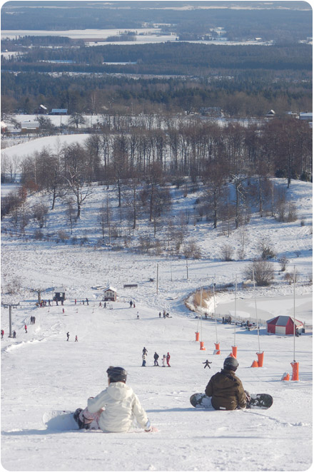 En snöklädd och pistad Kinnekullebacke med skidåkare och snowboardåkare i alla åldrar.