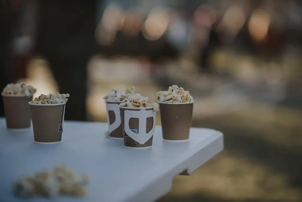 På kanten av ett vitt plastbord placerat utomhus så står några muggar fyllda med popcorn.