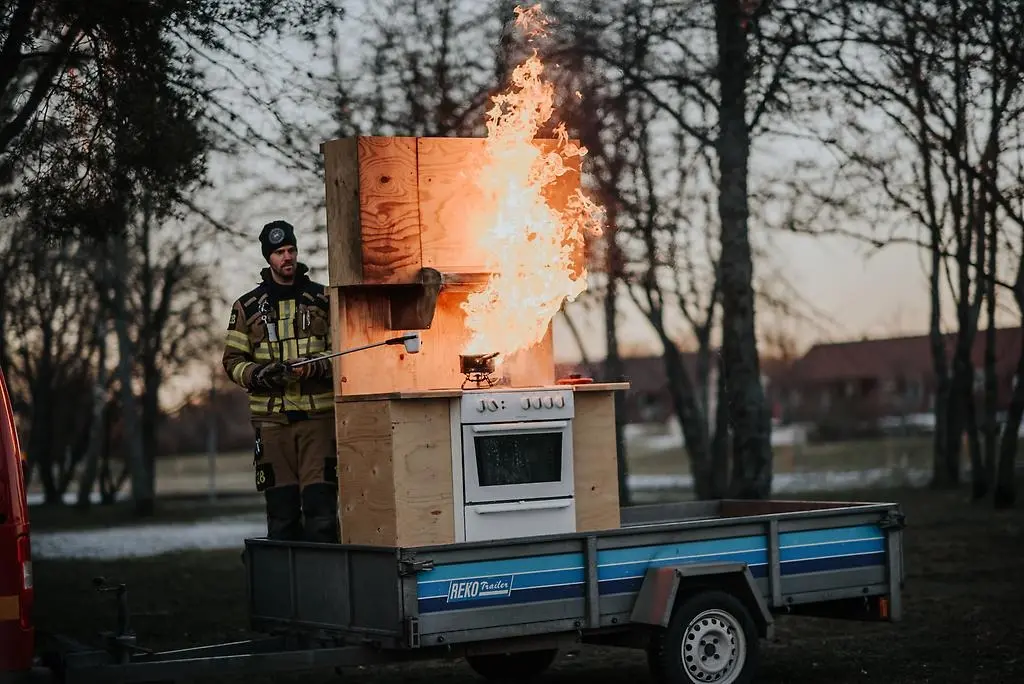 En brandman står bakom en portabel spis. Meterhöga eldsflammor syns efter att en oljebrand försökt släckas med vatten.