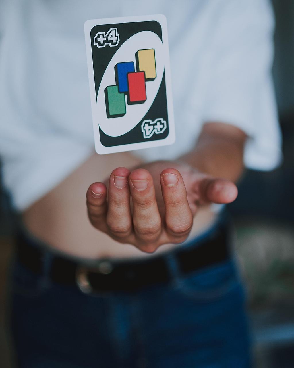 En hand som håller i ett uno-kort med 4 olika färger på kortet samt en 4+.