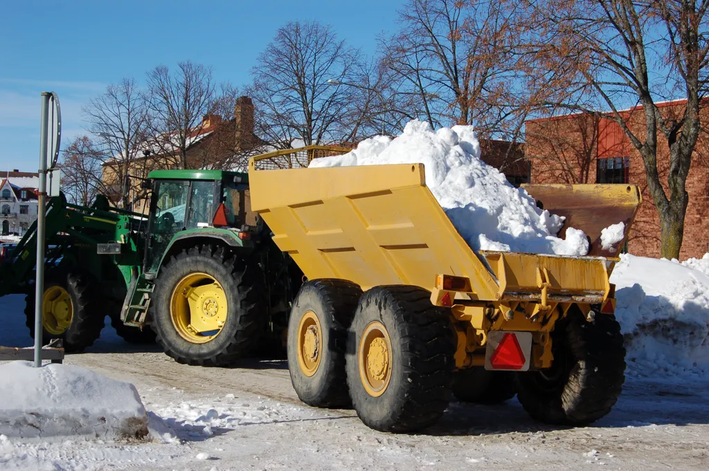 Traktor med flak som kör bort snö.