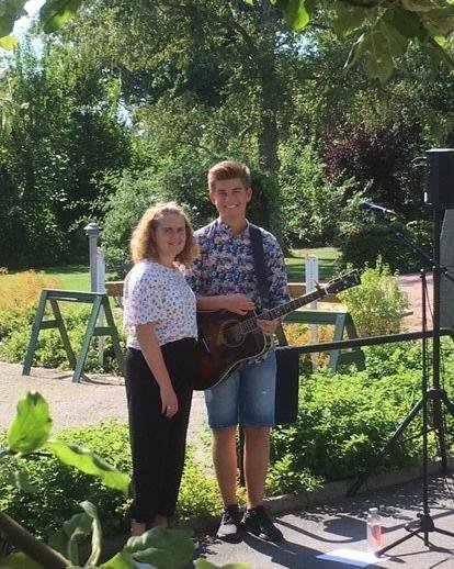 En tjej och en kille med gitarr står i en trädgård.