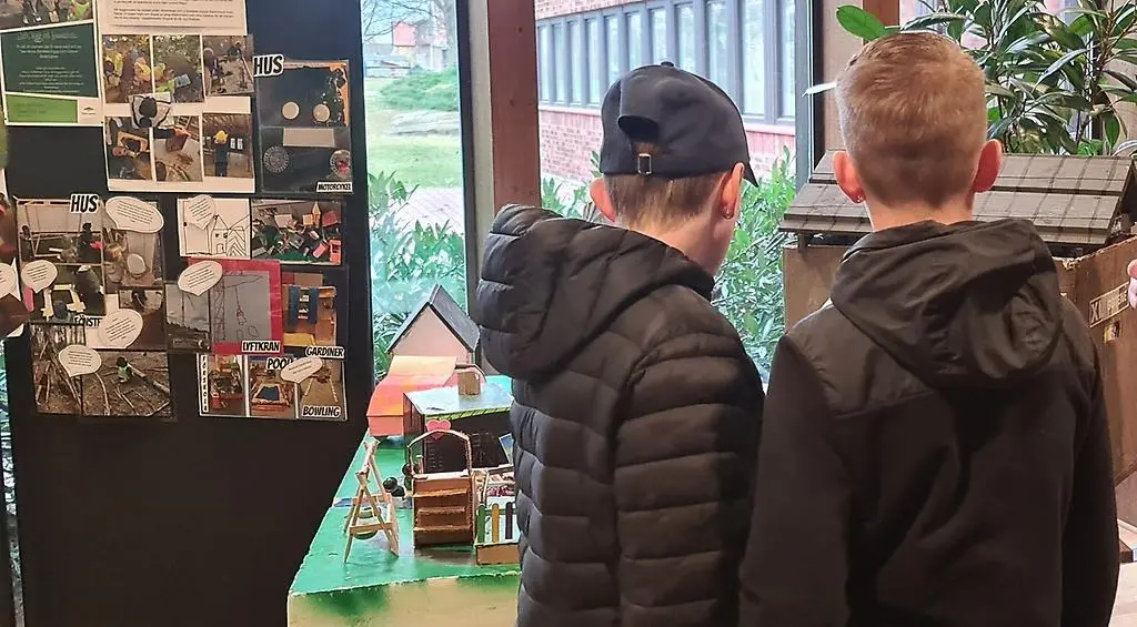 Två tonårskillar som står framför hus i kartong gjorda av förskolebarn.