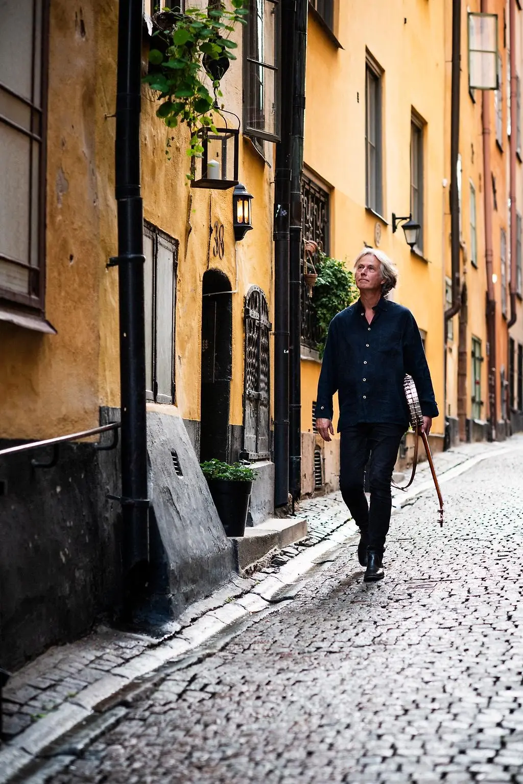 Dag går nedför en gränd med kullersten, med sin banjo i handen.