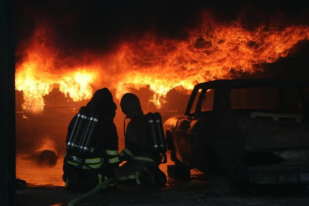 Två brandmän i rökdykarutrustning framför ett eldhav.