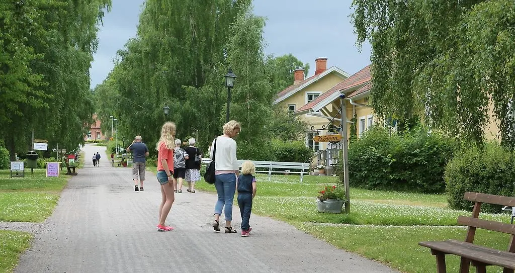 Promenadstråk med människor i grönskande miljö och hus i bakgrunden.