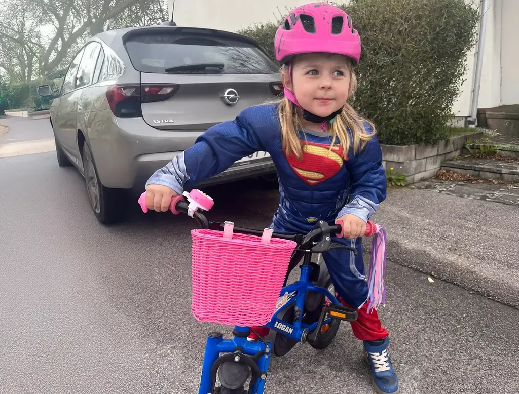 Liten tjej på cykel iförd stålmannendräkt.