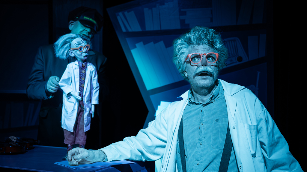 Ett foto som visar en man i orange glasögon och vit laboratorierock sittandes vid ett skrivbord på kvällen.