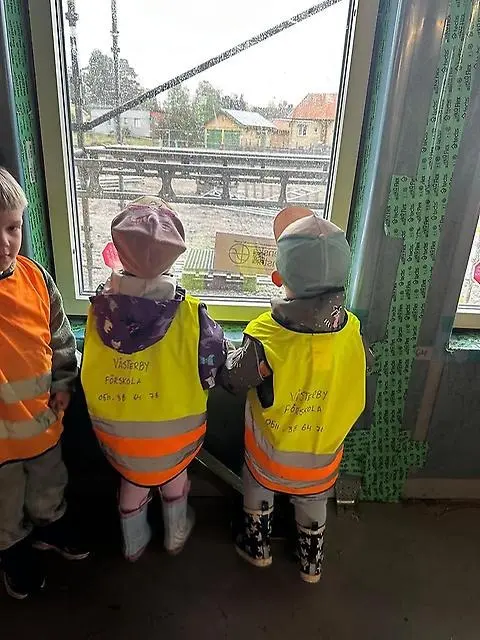 Två små barn i reflexvästar tittar ut genom ett fönster.