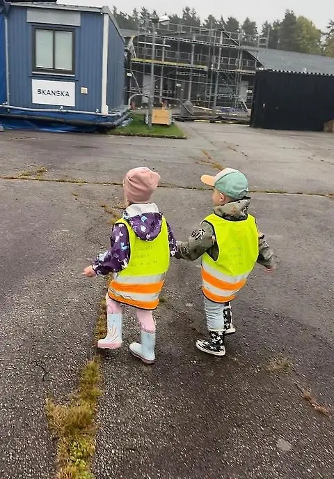 Två barn i reflexvästar håller handen och går runt på bygget.