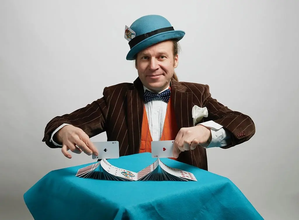 En man i kostym och hatt står framför ett bord och grejar med en kortlek.