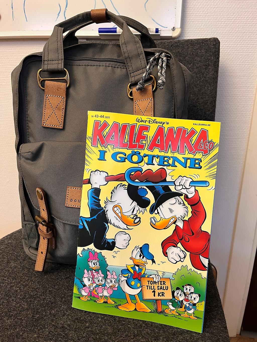 Kalle Anka-tidning som står lutad mot en ryggsäck på en stol.