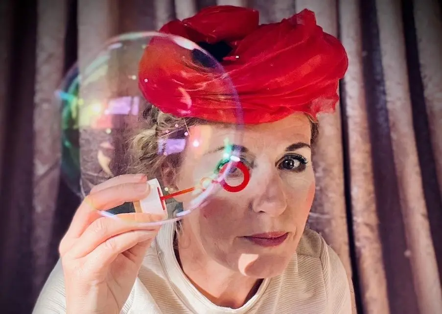 En kvinna i röd hatt håller upp en stor såpbubbla framför sig.