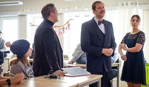 Klassrum med två mån och en kvinna med elever bakom sig.