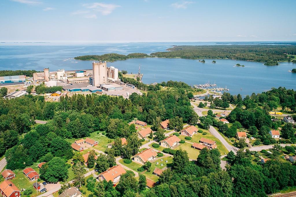 Flygbild över Hällekis samhälle: tak på boningshus, Parocs fabrik och Vänern i bakgrunden. 