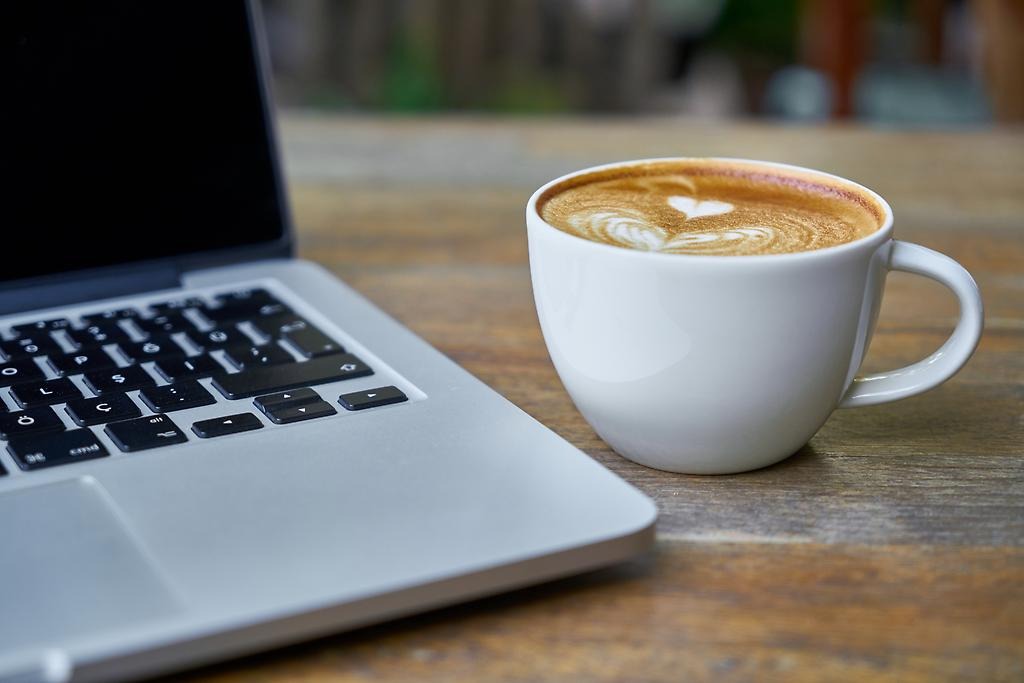 En vit kaffekopp står bredvid en laptop.