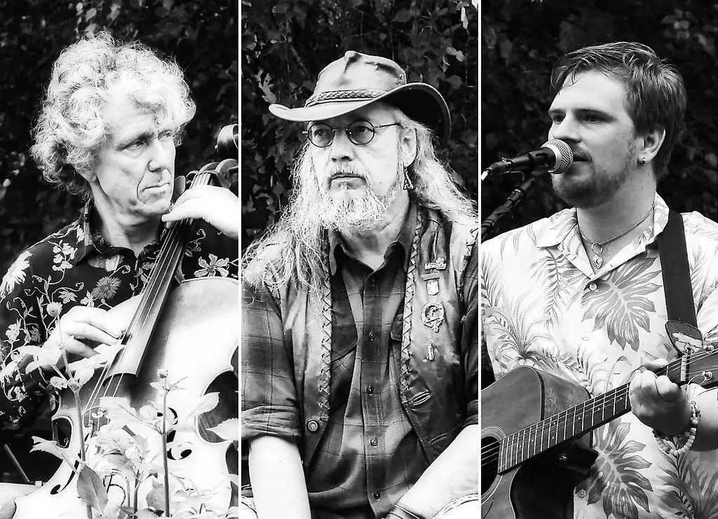 Tre män som alla spelar varsitt instrument. De står på rad och spelar kontrabas, trummor och gitarr. En av männen sjunger i en mikrofon.