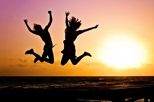 Silhuetterna av två glada ungdomar som hoppar framför en solnedgång.