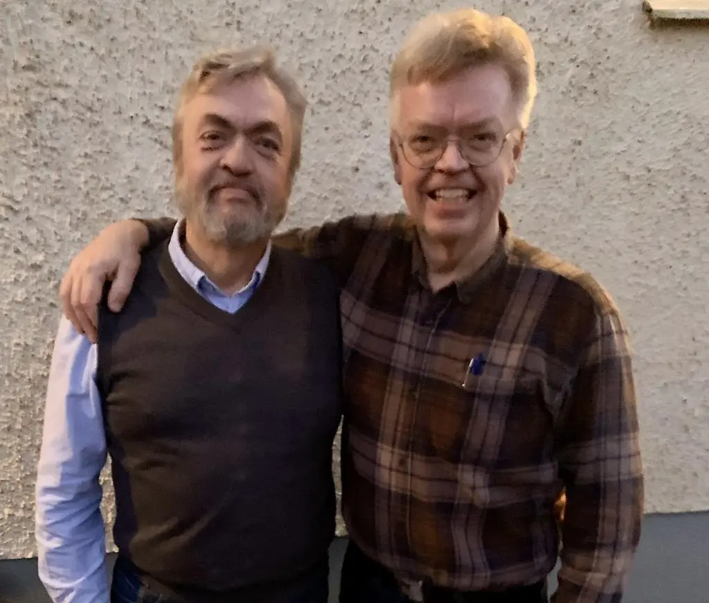Två män som håller varandra om axlarna och ler mot kameran.