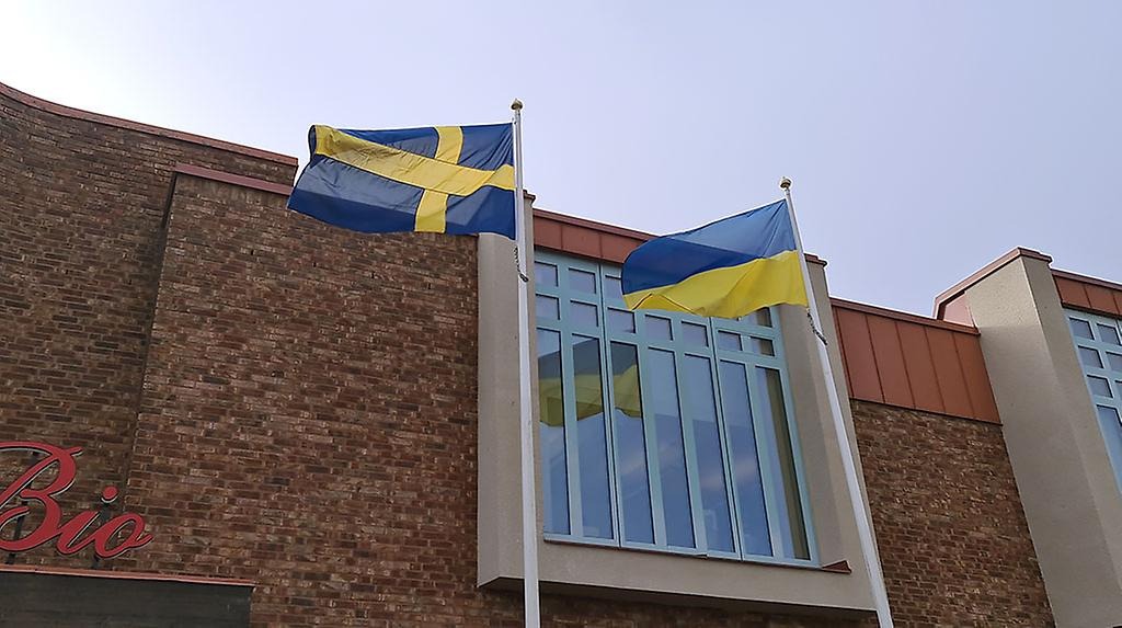 Svenska och ukrainska flaggan hissad framför en orange tegelvägg med ett stort fönster.
