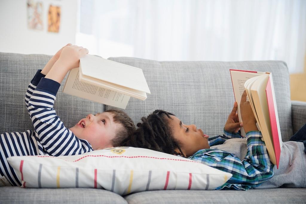 Två barn ligger i en soffa och läser i varsin bok. 