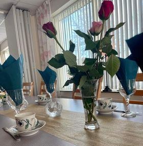 Dukat bord med kaffekoppar och assietter och en vas med röda rosor i. 
